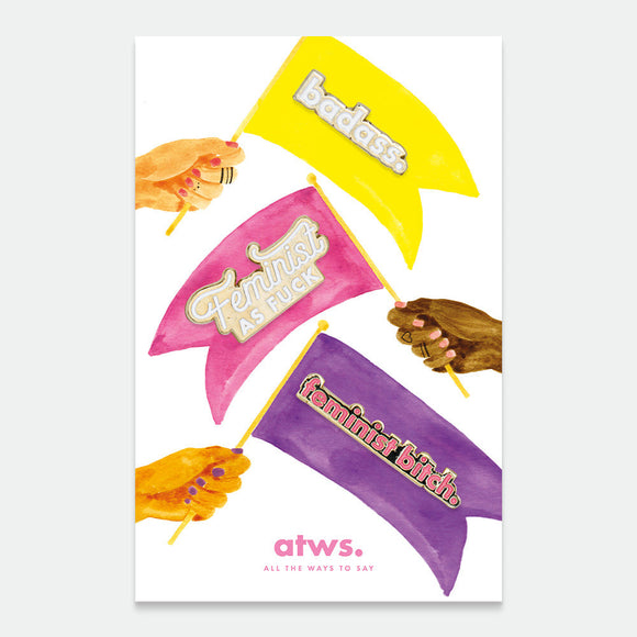 A set of three enamel pins with gold plating, each pin with a bold, empowering phrase written on it in black lettering, against yellow, pink, and purple backgrounds.