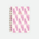 A spiral notebook with a white cover featuring a pattern of pink cats in various playful poses.
