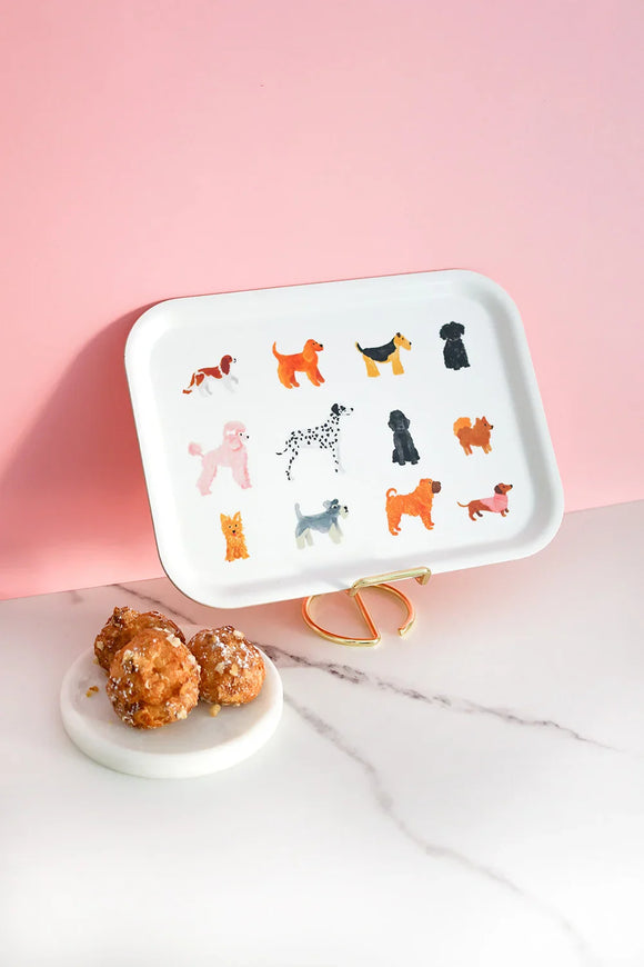 Rectangular white tray featuring illustrated dogs of different breeds and colors, styled on a pink background with pastries on a marble surface.