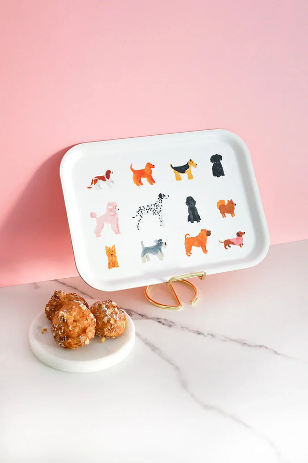 Rectangular white tray featuring illustrated dogs of different breeds and colors, styled on a pink background with pastries on a marble surface.