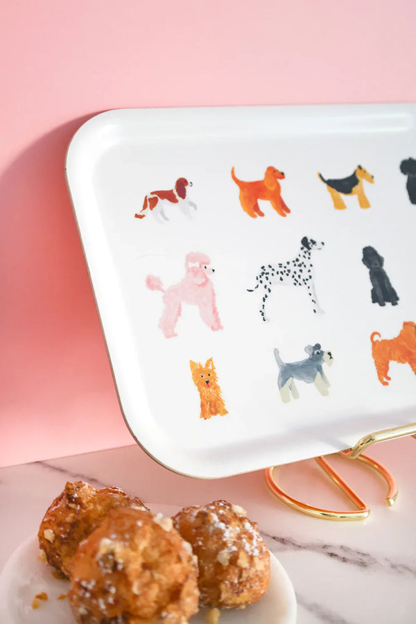 Close-up of a rectangular tray decorated with colorful dog illustrations, displayed with pastries on a marble table and pink backdrop.