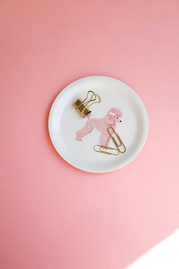 Small round tray featuring a pink poodle illustration on a pastel pink background, styled with gold stationery clips — All the Ways to Say.