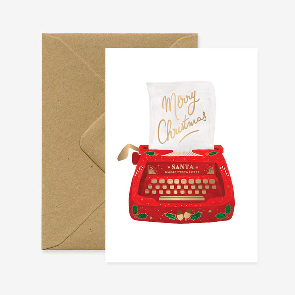A Christmas themed greeting card featuring a red typewriter with 'Santa' written on it, surrounded by holiday decorations, accompanied by a brown envelope.