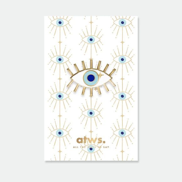 A radiant blue lucky eye enamel pin by All The Ways To Say with gold rays, displayed on a matching patterned backing card.