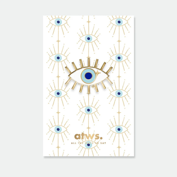 A radiant blue lucky eye enamel pin by All The Ways To Say with gold rays, displayed on a matching patterned backing card.