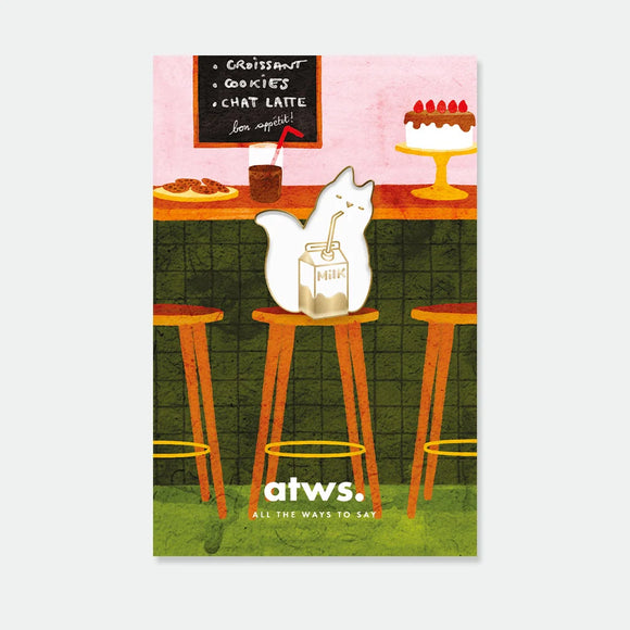 A cute gold enamel pin by All The Ways To Say showing a white cat drinking from a milk carton, displayed on a café-themed backing card.