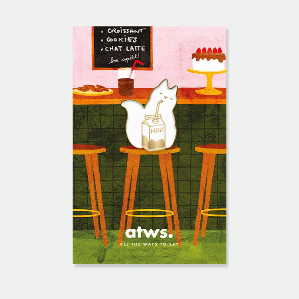 A cute gold enamel pin by All The Ways To Say showing a white cat drinking from a milk carton, displayed on a café-themed backing card.