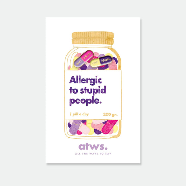 A duo of small gold enamel pins shaped like colorful capsules with the text "anti idiots", displayed on a pill jar themed card.