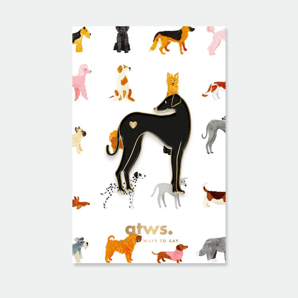 A sleek black greyhound enamel pin by All The Ways To Say with a small gold heart, displayed on a dog-themed grid backing card.