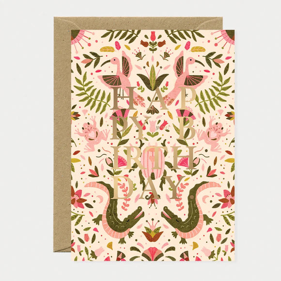 A symmetrical watercolor greeting card by All The Ways To Say featuring pink crocodiles, birds, and frogs with gold "HAPPY BIRTHDAY" text.