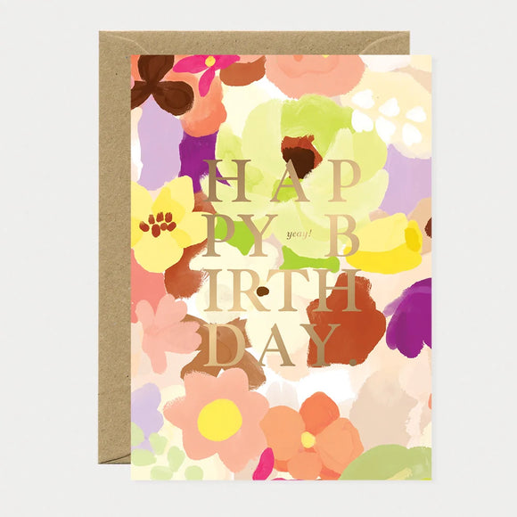 A vibrant floral greeting card by All The Ways To Say featuring the text "HAPPY BIRTHDAY" in gold lettering over a colorful watercolor background of spring flowers.