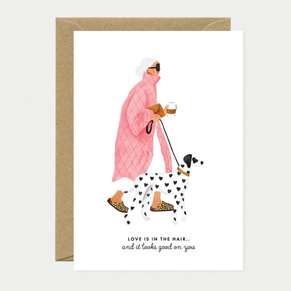 A chic greeting card by All The Ways To Say featuring a watercolor illustration of a woman in a pink quilted coat walking a heart-spotted dalmatian.