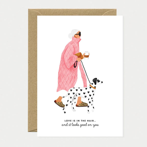 A chic greeting card by All The Ways To Say featuring a watercolor illustration of a woman in a pink quilted coat walking a heart-spotted dalmatian.