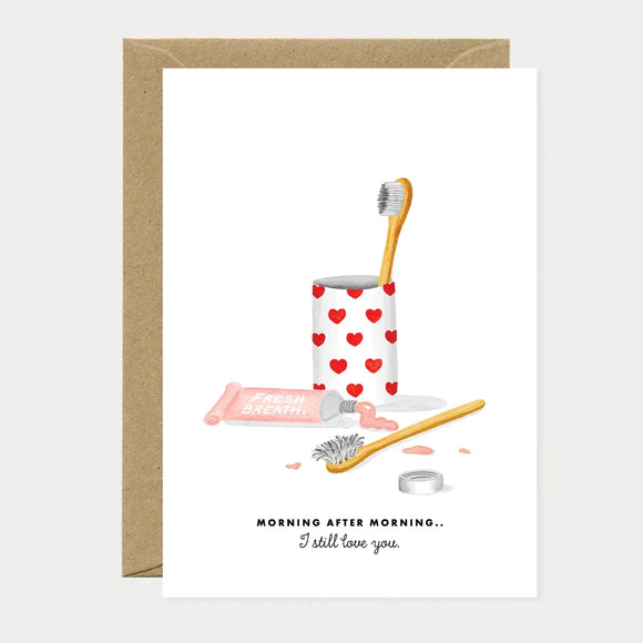 A romantic watercolor greeting card by All The Ways To Say featuring two toothbrushes in a heart-patterned cup and a tube of toothpaste with the text "MORNING AFTER MORNING.. I still love you."