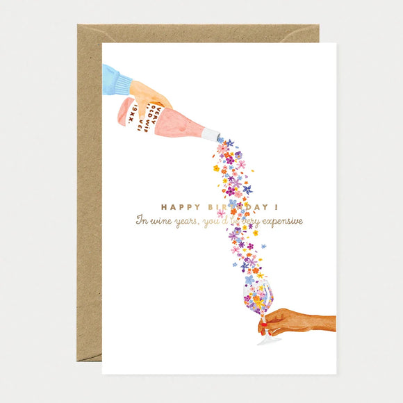 A poetic watercolor greeting card by All The Ways To Say showing a hand pouring a stream of flowers from a wine bottle into a glass with a birthday message.