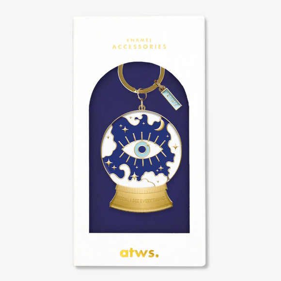 A mystical gold enamel keychain by All The Ways To Say in the shape of a crystal ball with an eye and the text "BITCH, I SEE EVERYTHING.", in its gift box.
