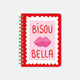 A large red spiral notebook by All The Ways To Say featuring a pink stamp with lips, the text "BISOU BELLA", and gold foil details.