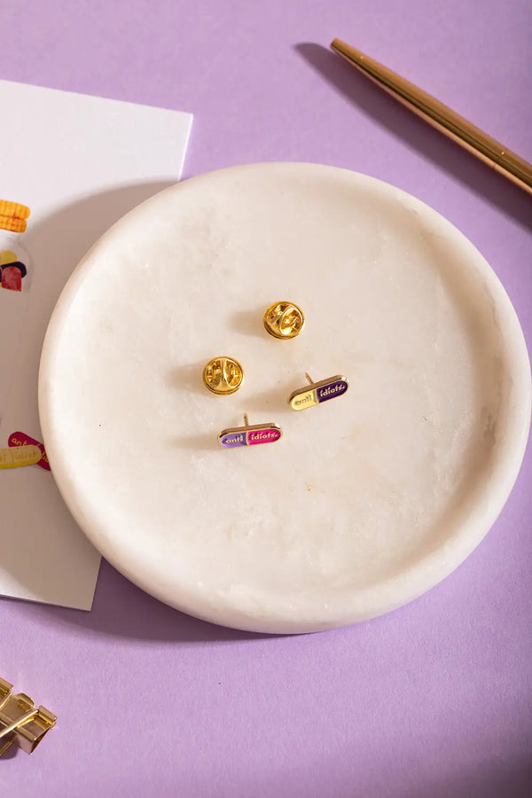 Duo Anti Idiots - Pins: overhead shot of the purple-pink and yellow-purple pill pins on a white tray.