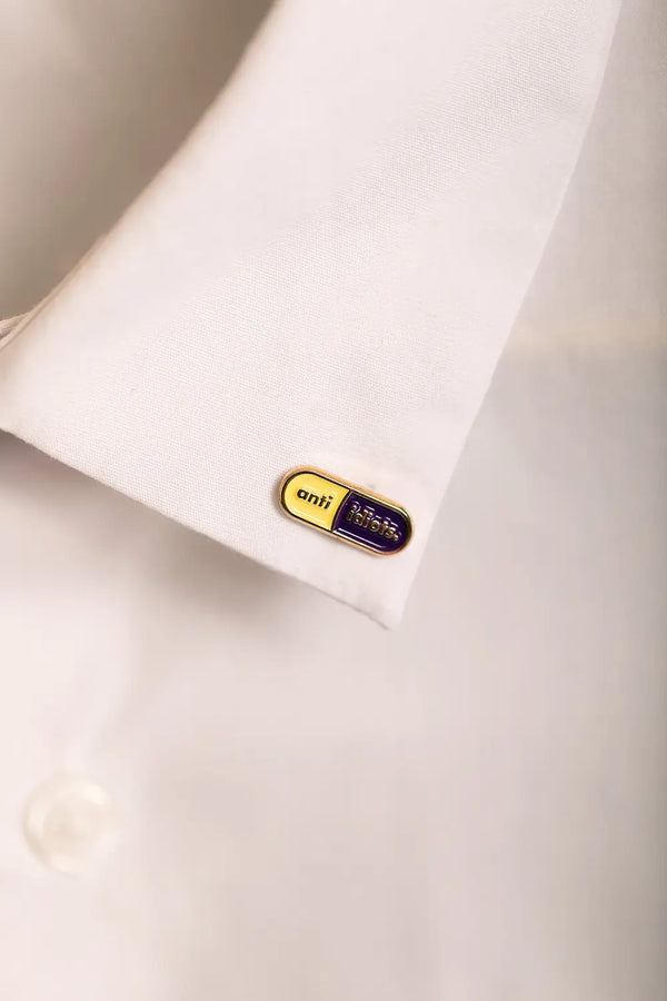 Duo Anti Idiots - Pins: the yellow and purple pill pin worn stylishly on a white shirt collar.
