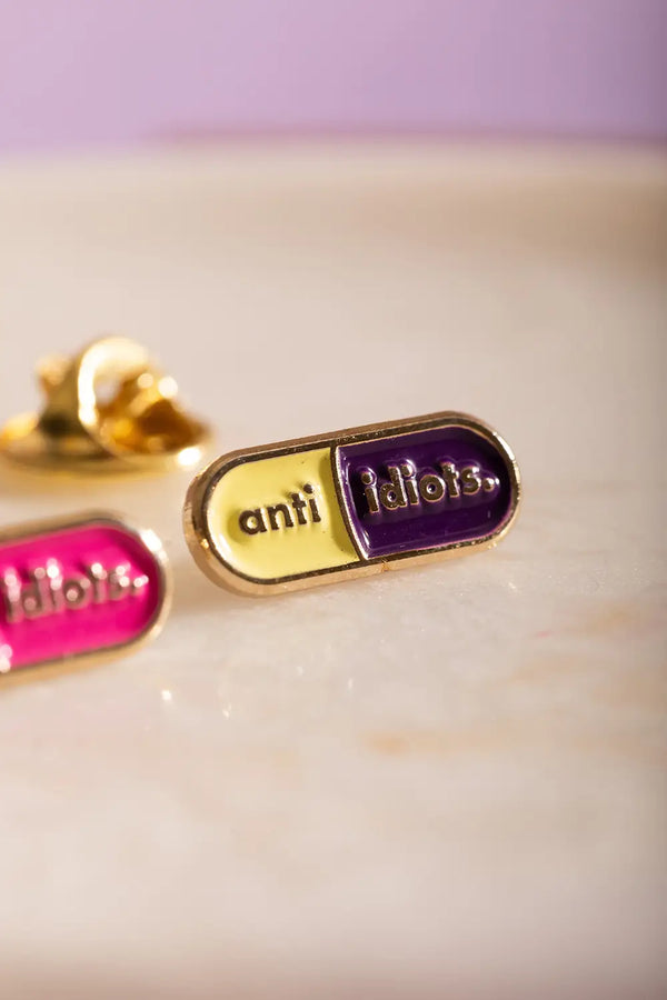 Duo Anti Idiots - Pins: macro shot of the yellow and dark purple "anti idiots" capsule pin.