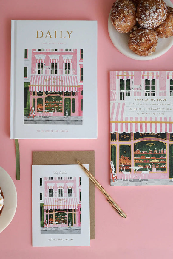 Flat lay of The Baguetter stationery collection featuring notebooks, card and coffee cup on a pink background