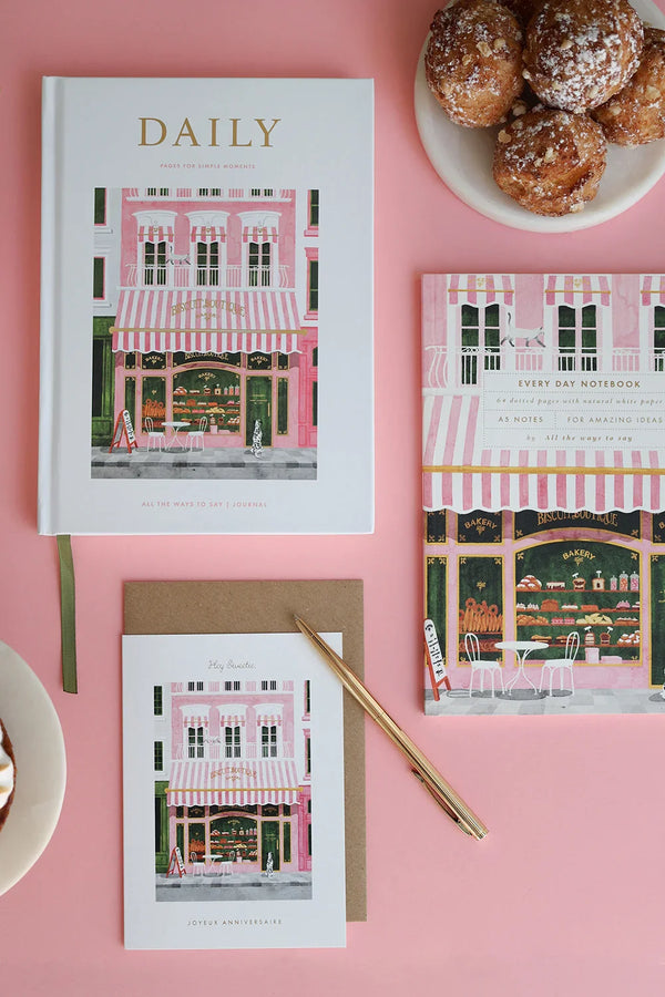 Flat lay of The Baguetter stationery collection featuring notebooks, card and coffee cup on a pink background