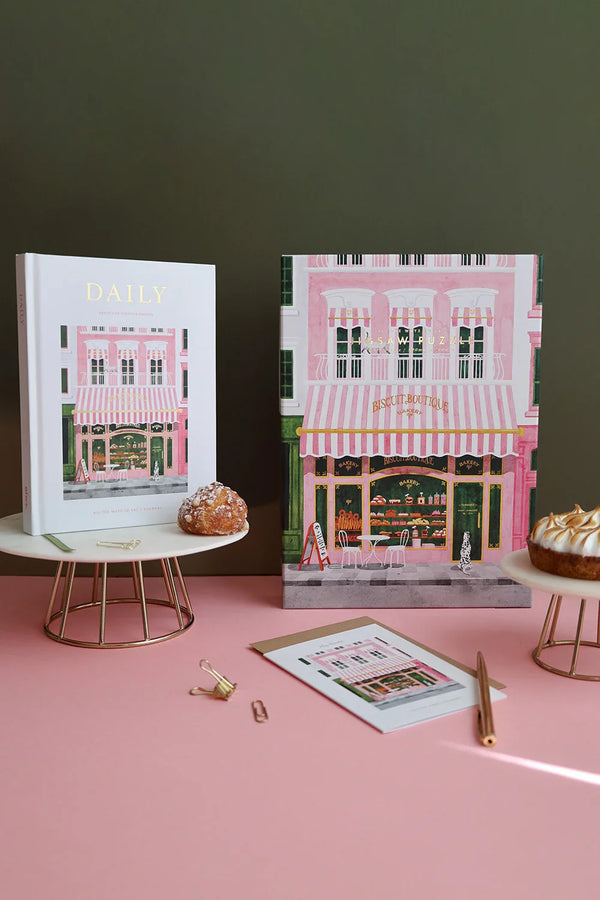 Close-up of The Baguetter stationery set including a journal, notebook and greeting card on pink surface