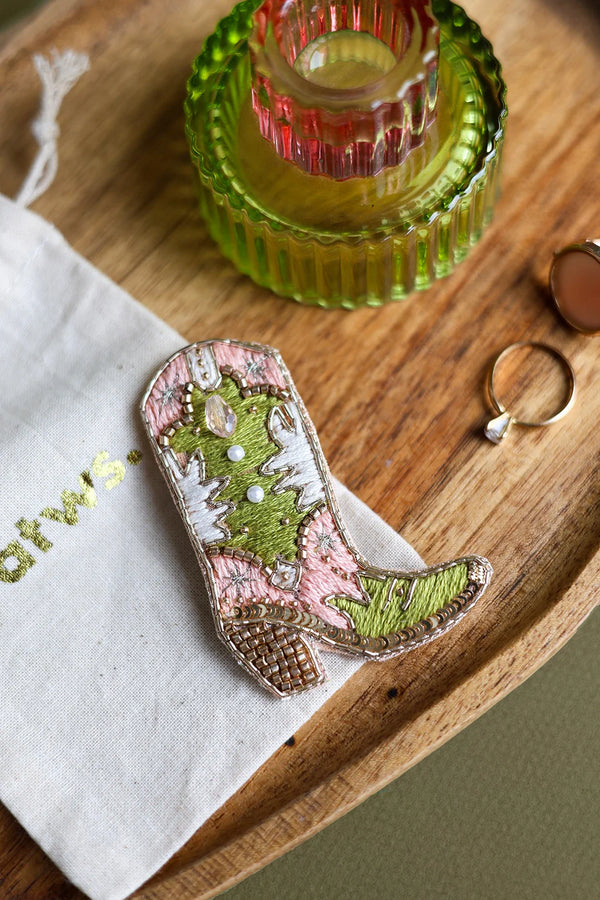 Top view of a western-style boot pin featuring intricate beadwork and embroidery on a wooden tray next to a cotton pouch.