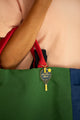 Blue "In my padel era" enamel keychain shaped like a padel racket, hanging from the red strap of a green tote bag