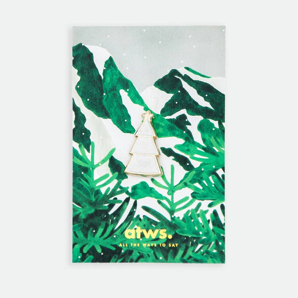 White Christmas Tree enamel pin by All the Ways to Say featuring gold-plated white tree with star detail on illustrated snowy mountain background with green pine branches.