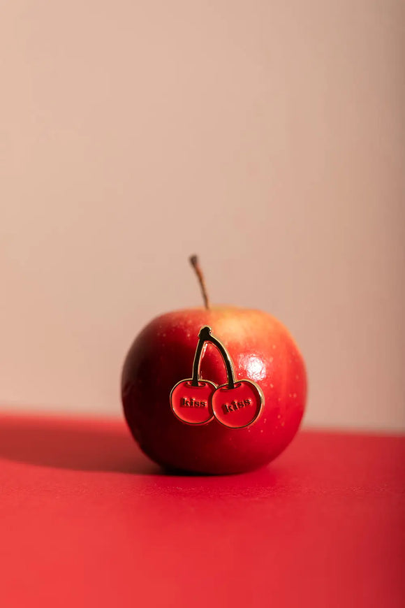 Kiss Kiss - Pins: the cherry "Kiss" pin creatively displayed on a fresh red apple.
