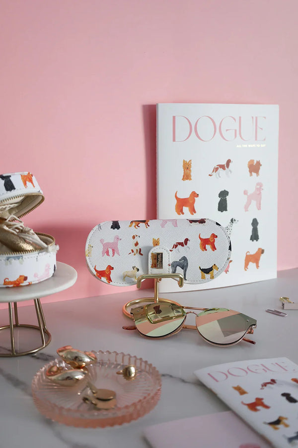 Dog-pattern glasses case styled with sunglasses, jewelry tray, and Dogue stationery on a marble table.