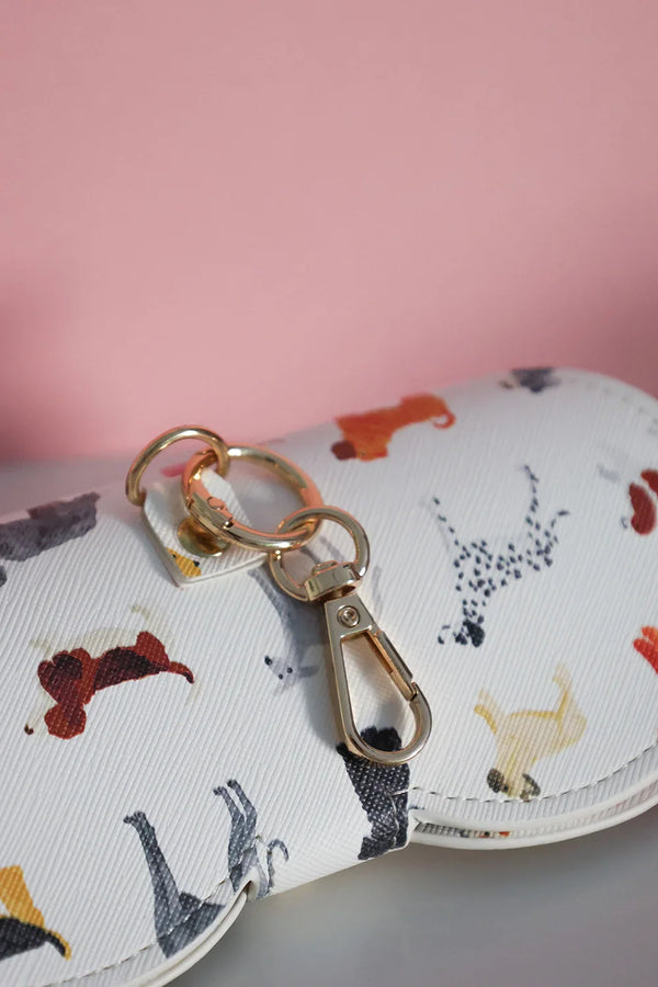 Close-up of dog-pattern glasses case with gold keychain clasp detail.