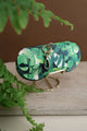 Green Cliff sunglasses case with tropical leaves print, gold clasp and keyring, displayed on marble stand with fern background.