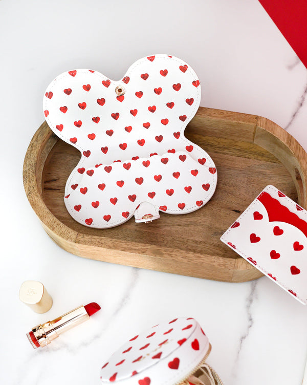 Open red hearts patterned glasses case displayed on a wooden tray with lipstick and matching card holder nearby