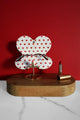 White glasses case with red heart pattern opened on a wooden stand, displayed with a red lipstick against a deep red background.