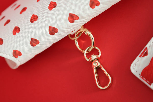 Close-up of a red hearts patterned glasses case with golden clasp detail on a red background