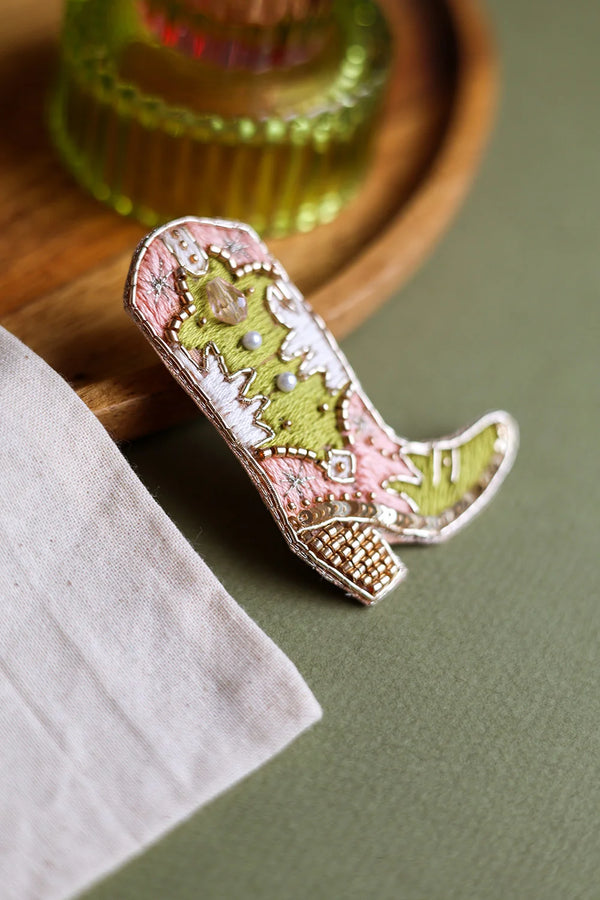 Macro shot of the cowboy boot brooch highlighting the sparkling sequins, crystal accents, and detailed gold wire embroidery.