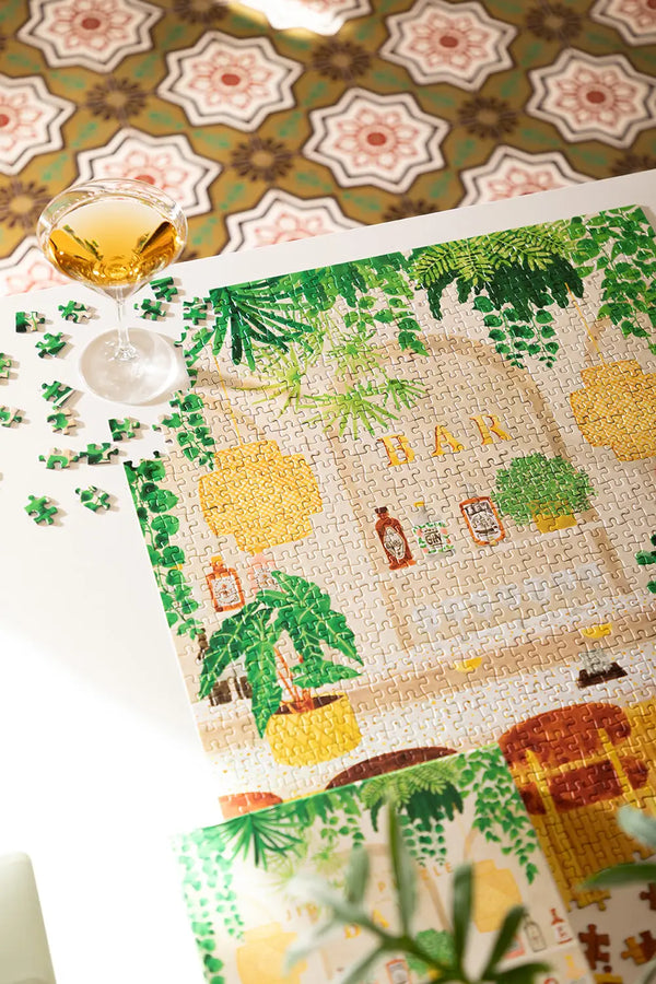 Bar - Puzzle 1000 pieces: a partially completed puzzle of a botanical bar scene next to a real cocktail.