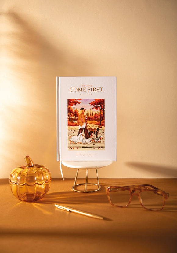"The dogs come first" A5 hardcover notebook, cover showing a woman walking dogs in Halloween costumes through an autumn park in New York