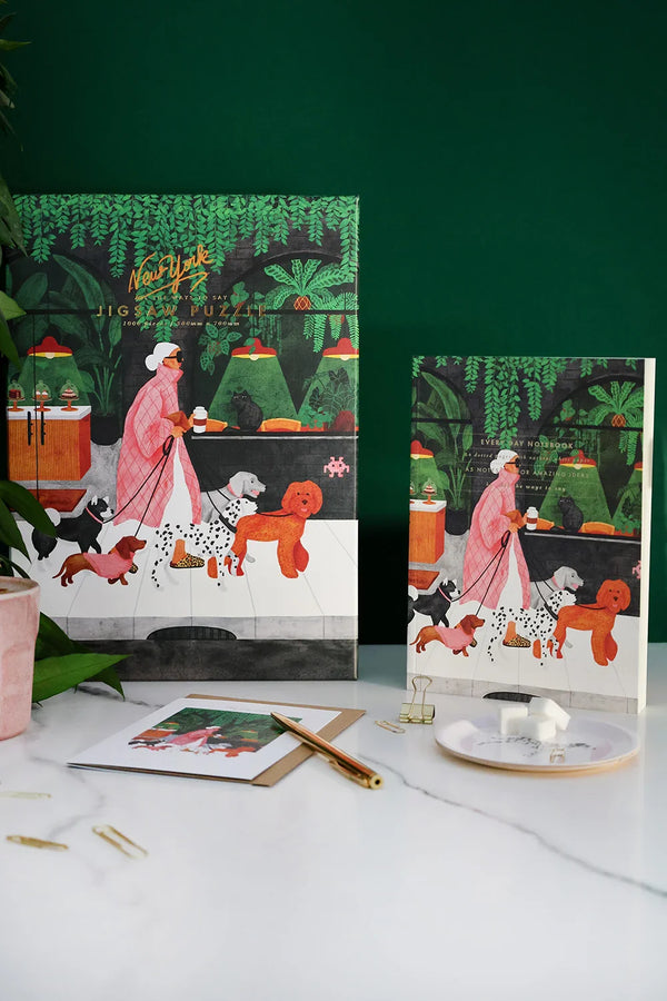 The Dog Sitter collection by All the Ways to Say – featuring the New York puzzle, tray, notebook, and greeting card with the iconic dog walker illustration in a cozy green setting.