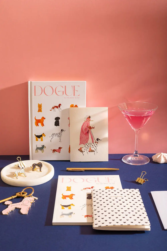 DOGUE - Collection: a stylish flat lay featuring "Dogue" notebooks, enamel pins, and a pink cocktail.