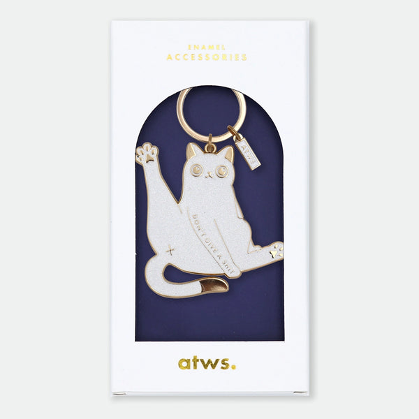 Enamel and metal keychain of a white cat mid-stretch with one paw raised, text engraved reading "Don't I give a sh*t," gold-tone ring and "ATWS" charm