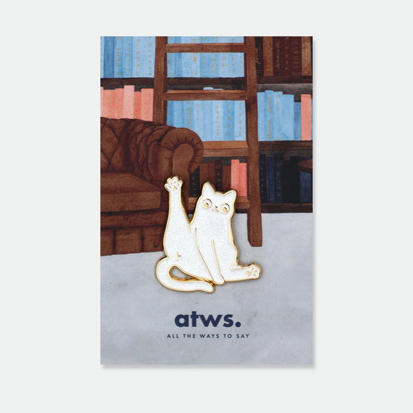 Enamel pin of a white cat mid-stretch with one paw raised, gold outline, text engraved along the side