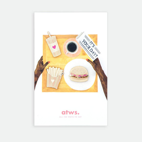 Junk Food XL enamel pin by All the Ways to Say featuring gold-plated burger, fries and drink design on illustrated tray background with newspaper and coffee.