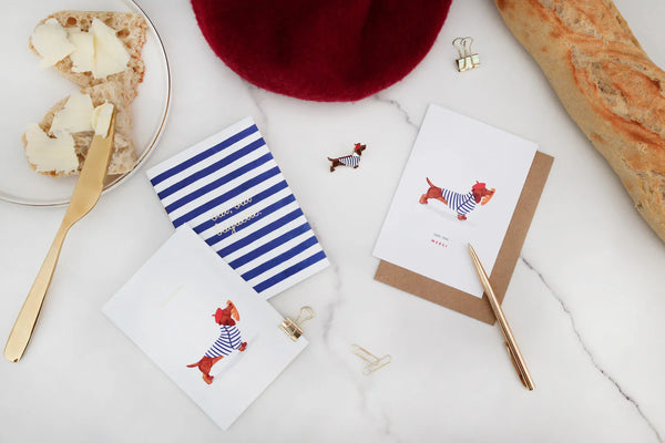 Frenchie collection by All The Ways To Say – Parisian flatlay with dachshund pin, striped notebook, baguette and butter breakfast