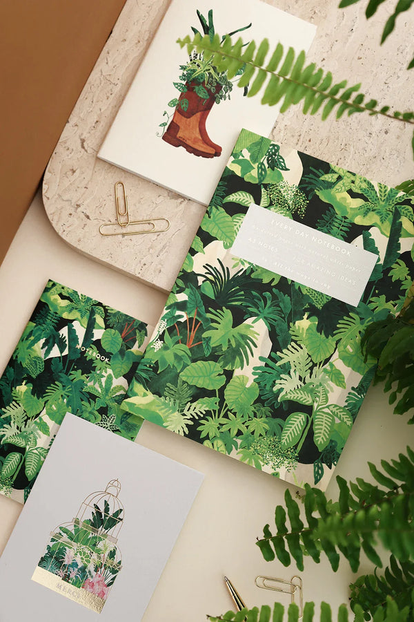 Green Cliff botanical notebooks and stationery with lush jungle leaf patterns, surrounded by ferns.