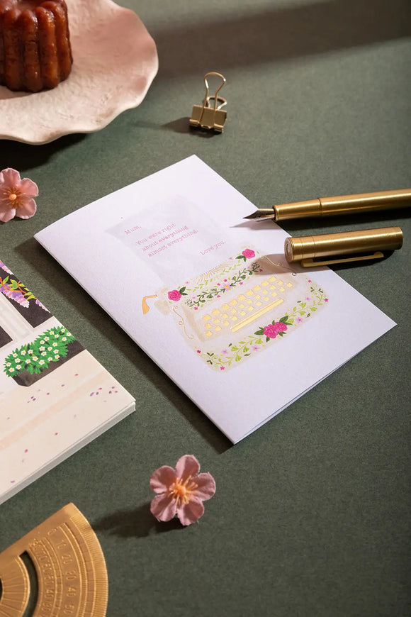 Love you mum typewriter Greeting card - Lifestyle view with a floral typewriter illustration on a green desk.