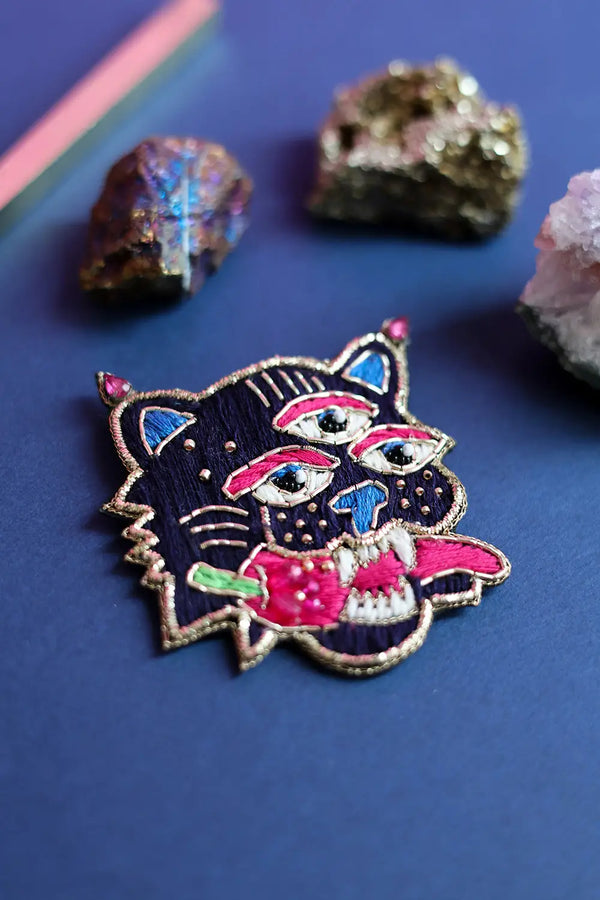 Vibrant maximalist tiger face brooch surrounded by raw pyrite and amethyst crystals, showcasing a bohemian luxury aesthetic.