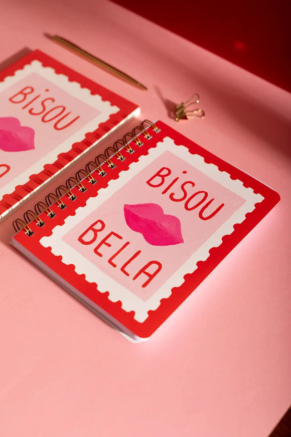 Bisous Bella Spiral Notebook - Front view on a pink desk with a gold pen and clip.